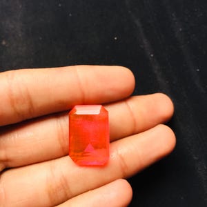 Op de afbeelding: Een rechthoekige, gefacetteerde edelsteen met een levendige, doorschijnende neonoranje tint. De steen heeft een klassieke smaragdgeslepen vorm met strakke randen en een gepolijst oppervlak dat licht reflecteert en de heldere, verzadigde kleur benadrukt.