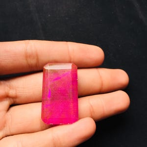 May include: A rectangular gemstone with a vibrant hot pink hue and a faceted surface. The stone features a polished finish that reflects light, showcasing a deep, saturated color throughout its structure. The edges are beveled and smooth.