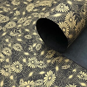 K&ouml;nnte beinhalten: Schwarzes Geschenkpapier mit goldenem Blumenmuster. Das Papier ist aufgerollt und das Muster ist auf der Au&szlig;enseite der Rolle sichtbar.