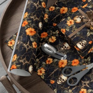 Puede incluir: Papel de regalo de Halloween negro y naranja con un patrón de calavera y flores. El papel está enrollado y hay una caja de regalo envuelta en el mismo papel.