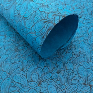 May include: A roll of turquoise paper with a repeating pattern of brown, swirling, organic shapes. The paper is partially rolled, revealing the underside. The design creates a flowing, textured appearance.