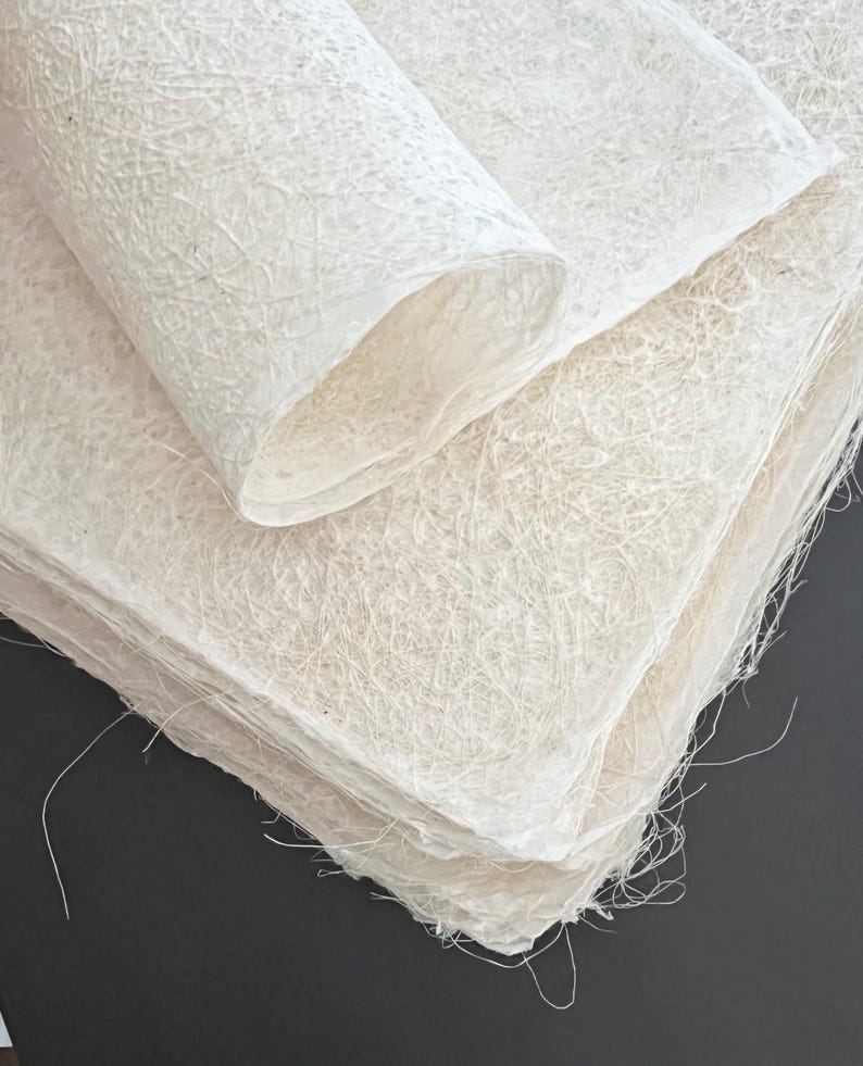 Op de afbeelding: Een stapel wit handgemaakt papier met een textuur. Het papier is bovenaan opgerold, waardoor de vezels zichtbaar worden.