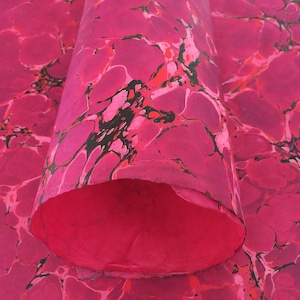 May include: A sheet of paper with a marbled pattern in shades of vibrant pink, magenta, and black. The paper is rolled into a cylindrical shape, revealing a solid pink interior, while the exterior displays a swirling, organic marbled design.