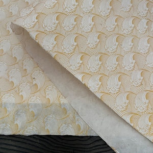 Pode incluir: Uma folha de papel branco com um padrão repetitivo de ondas douradas. O papel está dobrado ao meio e as bordas estão ligeiramente desfiadas.