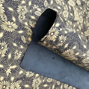 K&ouml;nnte beinhalten: Eine schwarze Yogamatte mit einem floralen Muster in Gold. Die Matte ist aufgerollt und das Blumenmuster ist auf der Au&szlig;enseite der Rolle sichtbar.