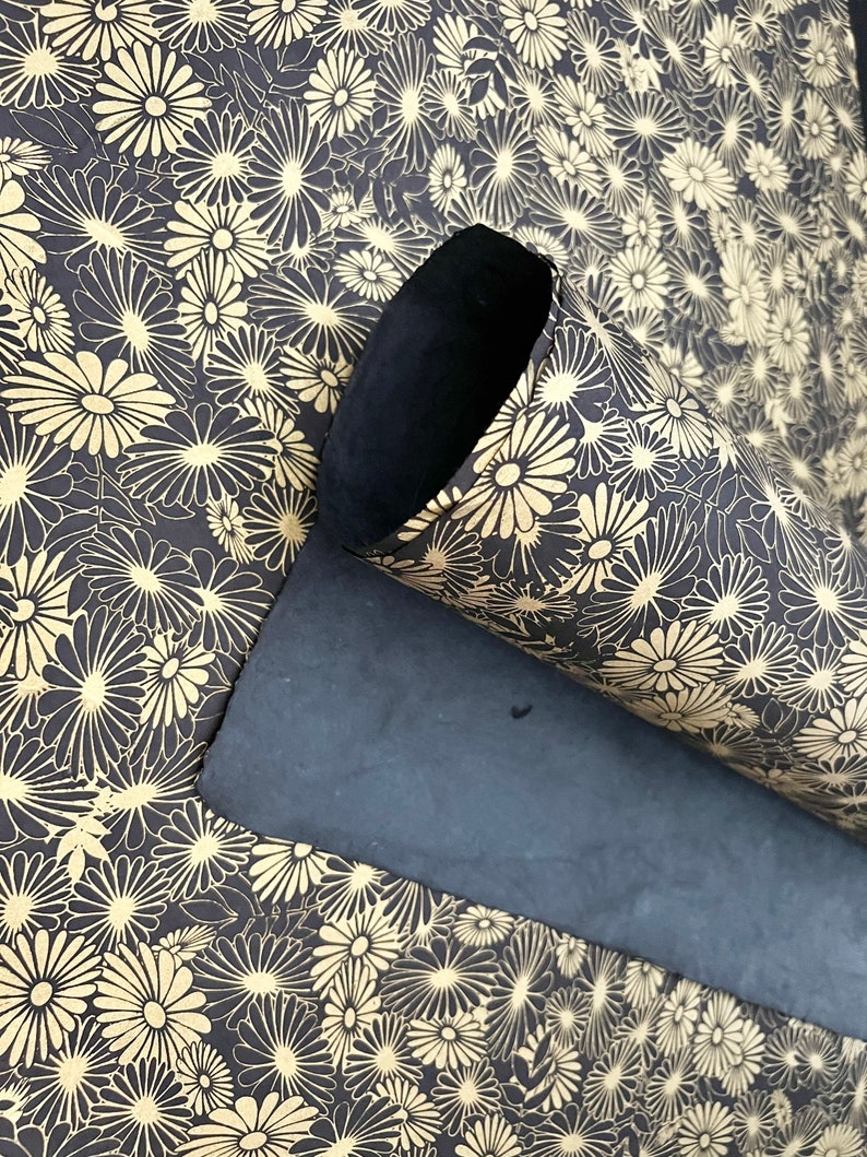 K&ouml;nnte beinhalten: Eine schwarze Yogamatte mit einem floralen Muster in Gold. Die Matte ist aufgerollt und das Blumenmuster ist auf der Au&szlig;enseite der Rolle sichtbar.