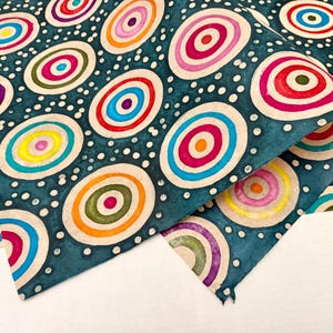 May include: A teal-colored fabric with a repeating pattern of colorful concentric circles. The circles are in shades of red, pink, yellow, blue, and green, with white dots scattered throughout. The fabric is folded over, revealing the pattern.