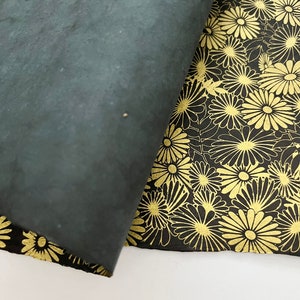 K&ouml;nnte beinhalten: Zwei St&uuml;cke schwarzes Papier mit einem goldenen Blumenmuster. Ein St&uuml;ck ist &uuml;ber das andere gefaltet und zeigt das Muster.