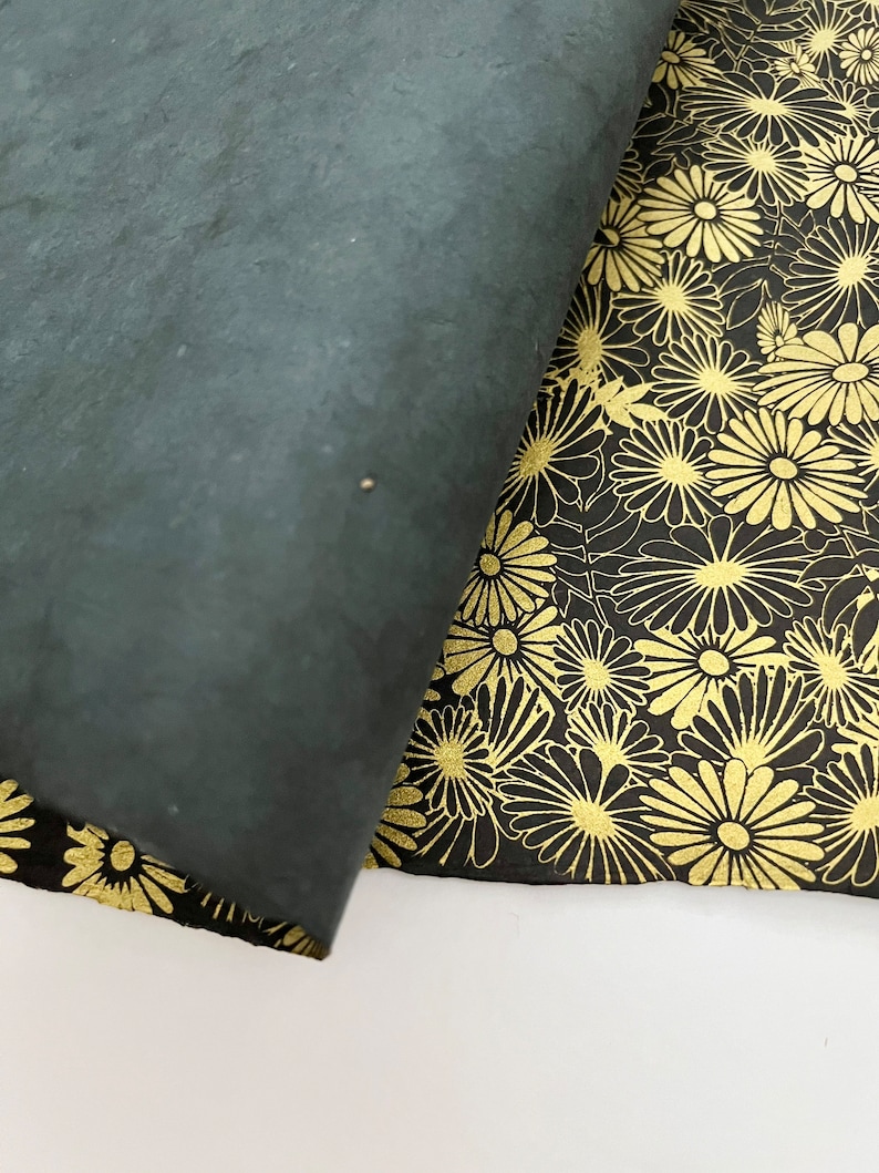 K&ouml;nnte beinhalten: Zwei St&uuml;cke schwarzes Papier mit einem goldenen Blumenmuster. Ein St&uuml;ck ist &uuml;ber das andere gefaltet und zeigt das Muster.
