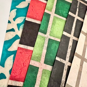 May include: Four sheets of decorative paper with different patterns. The first sheet is teal blue with a white floral design. The second sheet is red with black and white squares. The third sheet is green with black and white squares. The fourth sheet is beige with gray and white squares.