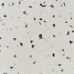 May include: White paper with a scattered pattern of small, pressed, dried flowers in shades of pink, purple, and blue.