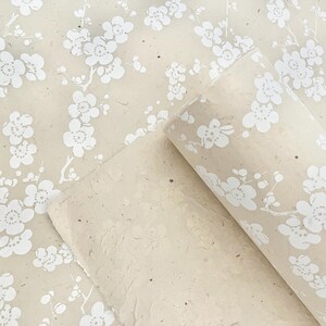 Puede incluir: Un rollo de papel de regalo beige con un patr&oacute;n floral blanco. El papel est&aacute; hecho de materiales reciclados y tiene una superficie texturizada.