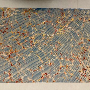 May include: Rectangular sheet with a marbled design. The background is a light blue with diagonal lines. The marbled pattern features red, yellow, and white veins, creating a unique and textured appearance. The edges are slightly uneven.