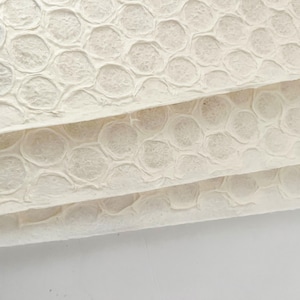 Op de afbeelding: Close-up van een stapel wit textuurpapier met een reliëfpatroon van cirkels. Het papier heeft een zachte, organische uitstraling.