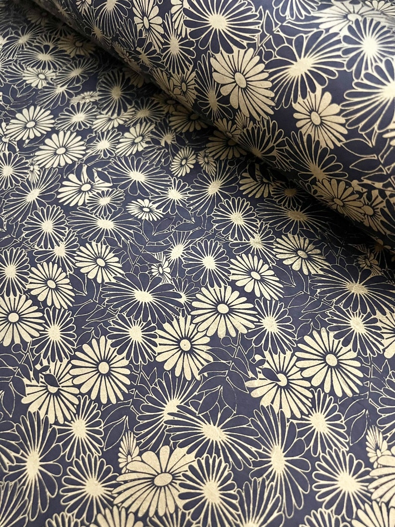 K&ouml;nnte beinhalten: Ein schwarzes und goldenes Geschenkpapier mit floralem Muster und einem sich wiederholenden Design aus stilisierten Blumen. Das Papier ist aufgerollt und das Muster ist sowohl auf der Vorder- als auch auf der R&uuml;ckseite der Rolle sichtbar.