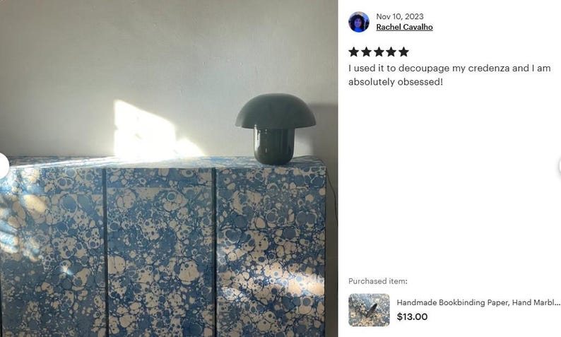 May include: A rectangular credenza covered in blue and white marbled paper with a swirling pattern, featuring a dark green mushroom-shaped lamp placed on top. The surface displays a complex mix of blue tones and white circular shapes.