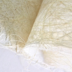 Op de afbeelding: Close-up van een wit, getextureerd, papierachtig materiaal met een delicate, vezelachtige structuur. Het materiaal is gemaakt van dunne, verweven draden die een delicate, luchtige uitstraling cre&euml;ren.