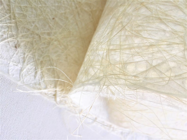 Op de afbeelding: Close-up van een wit, getextureerd, papierachtig materiaal met een delicate, vezelachtige structuur. Het materiaal is gemaakt van dunne, verweven draden die een delicate, luchtige uitstraling cre&euml;ren.