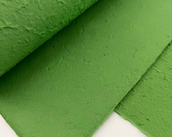 Puede incluir: Hojas de papel verde texturizado, enrolladas. El papel tiene un aspecto rugoso y hecho a mano.