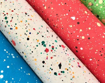 May include: Three rolls of wrapping paper with a splatter paint design. The rolls are in shades of blue, white, and red.