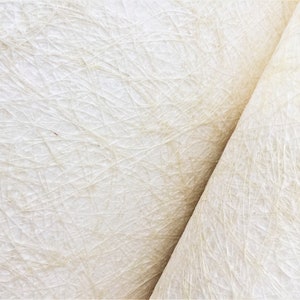 Op de afbeelding: Close-up van een wit, getextureerd papier met een subtiel geweven patroon. Het papier is doormidden gevouwen, waardoor een diagonale lijn over de afbeelding loopt.