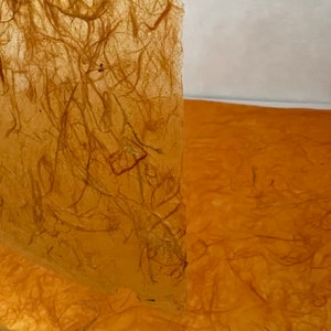 May include: A sheet of translucent, amber-colored paper with a visible fibrous texture. The material features an organic, tangled pattern of embedded golden-brown fibers throughout, creating a semi-transparent effect when light passes through the surface.
