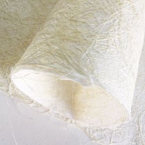 Op de afbeelding: Close-up van een vel wit, getextureerd papier met een delicaat, vezelig patroon. Het papier is dubbelgevouwen, waardoor het zachte, witte interieur zichtbaar wordt.