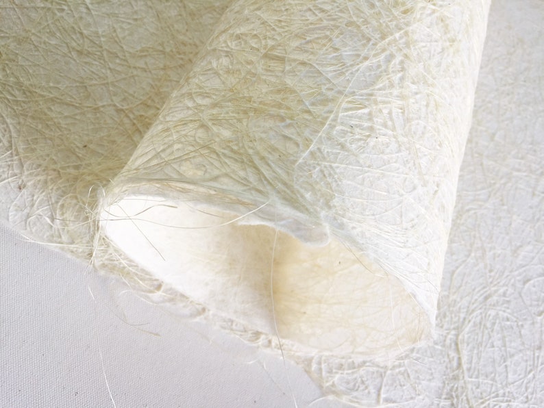 Op de afbeelding: Close-up van een vel wit, getextureerd papier met een delicaat, vezelig patroon. Het papier is dubbelgevouwen, waardoor het zachte, witte interieur zichtbaar wordt.