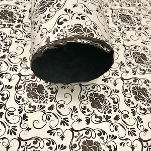 May include: A roll of white paper with a black damask pattern. The paper is rolled up and the end is visible.