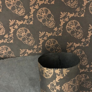 May include: A roll of black wrapping paper with a gold skull and floral pattern. The paper is rolled up and sitting on a piece of brown paper.