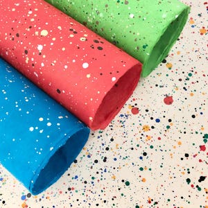 May include: Three rolls of colorful paper with a splatter paint design. The rolls are green, red, and blue. The paper is rolled up and the ends are visible.