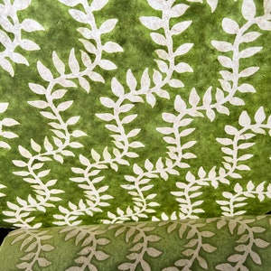 May include: Green paper with a white leaf pattern. The paper is rolled up and the pattern is visible on the outside of the roll.