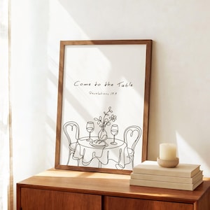 May include: A framed wall art print featuring a black line drawing of a table set for two with wine glasses, a vase of flowers, and a loaf of bread. The text reads Come to the Table and Revelations 19:9 in a simple, handwritten black font style.