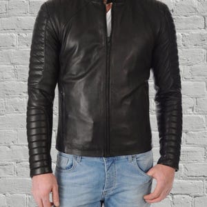 May include: Black leather jacket with a stand-up collar and a zip-up front. The jacket features quilted detailing on the shoulders and sleeves. The model is wearing light blue jeans.