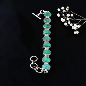 May include: A silver bracelet featuring nine oval-shaped green stones set in individual metal bezels. The bracelet includes a toggle clasp mechanism at one end and a series of circular links at the other, providing an adjustable fit for the wrist.