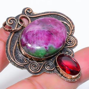 May include: An elaborate pendant with a large, oval pink and green gemstone as the focal point. A smaller, red oval stone is set below. The pendant has a detailed, swirling metalwork design in bronze and silver.