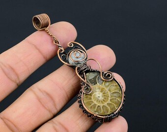 May include: A handcrafted pendant featuring a fossilized ammonite encased in copper wire. The pendant has a spiral design with shades of brown, tan, and copper. The wirework includes decorative swirls and a loop for a chain.