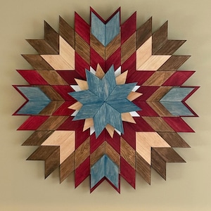 May include: A circular wooden wall art piece featuring a geometric star pattern. The design is composed of individual wooden segments stained in shades of deep red, dark brown, light beige, and a muted blue, arranged in a symmetrical starburst.