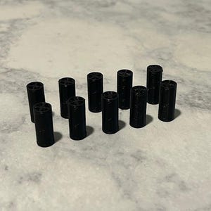 May include: A collection of ten black cylindrical objects, each with a patterned top. The objects are evenly spaced and appear to be made of a solid material. The lighting is soft, and the background is a neutral color.