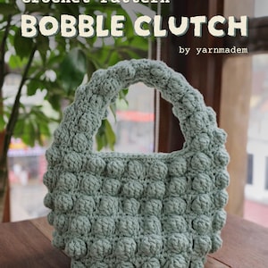 May include: A sage green crochet clutch with a textured bobble stitch design. The bag has a rounded shape with a handle and is displayed on a wooden surface. Text on the image reads "Crochet Pattern BOBBLE CLUTCH by yarnmadem."