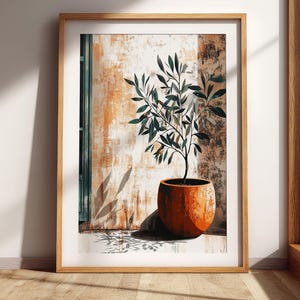 May include: A framed wall art print featuring a potted olive tree with dark green leaves in a round, textured terracotta-colored pot. The background shows a weathered, light orange and white wall with a vertical green panel and cast shadows.