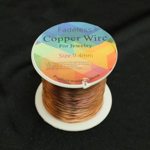 Könnte beinhalten: Eine Spule Kupferdraht für die Schmuckherstellung. Das Etikett lautet "Fadeless Copper Wire For Jewelry" mit einer Größe von 0,4 mm. Das Etikett hat ein farbenfrohes geometrisches Design. Der Draht hat eine warme Kupferfarbe.
