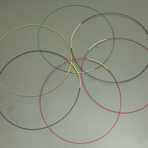 Könnte beinhalten: Eine Sammlung dünner, kreisförmiger Halsketten in verschiedenen Farben, darunter Gold, Schwarz, Rot, Grün und Silber. Die Halsketten sind kreisförmig angeordnet, wobei sich die Enden überlappen.