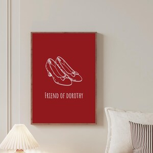 May include: A framed art print featuring a pair of white illustrated shoes on a red background. The text "FRIEND OF DOROTHY" is below the shoes. The artwork is displayed in a bedroom setting.