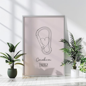 May include: A framed print featuring a minimalist line drawing of a carabiner with a heart inside. The words "Carabiner ENERGY" are written in a script font below the drawing. The background is a soft pink color.