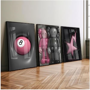 May include: Three framed artworks. The first shows a pink eight ball. The second displays two cartoon figures, one pink and one grey. The third shows a pink star. All are set against a grey background.