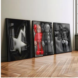 May include: Three framed art pieces featuring pop art figures and designs. The first frame has a white star shape, the second has two figures in red and gray, and the third has a black and white design with an 8-ball.