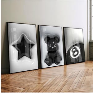 Peut inclure: Trois impressions d'art encadrées présentant des motifs en noir et blanc. Les impressions présentent une étoile noire, une figurine d'ours noire avec des X pour les yeux et une boule de billard noire et blanche. Les impressions sont exposées sur un sol en bois.