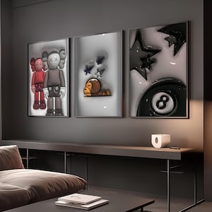 May include: Three framed art pieces with pop art designs. One features two cartoon figures, another a monkey with stars, and the last a black and white eight ball. The artwork is displayed above a dark brown table.
