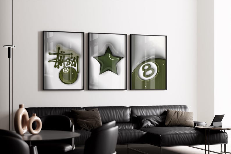May include: Three framed art prints with black frames. The prints feature a green and white color scheme with a Stussy logo, a star, and an eight ball design. The art is displayed above a black leather sofa.